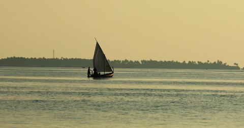 Maldives traditional sailboat, dhoni. Sunset on the ocean with people pointing and sailing with palm trees and ocean water on vacation in tourist destination, tropical island, summer holiday hotspot.