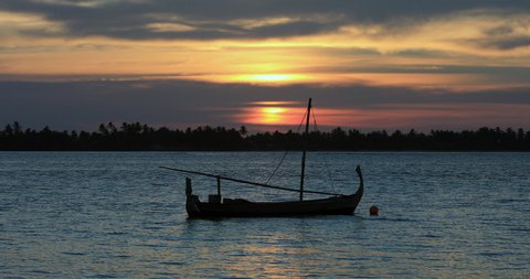 Sunset in Maldives with silhouette of sailboat dhoni. Dramatic palm trees and ocean waves, vacation, tourism holiday island for background graphics