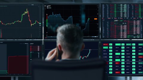 Trader is working with multiple computer screens full of charts and data analysis and stock broker trading online. Back view. Concept of bitcoin and stock market trading.