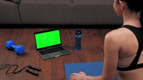 Fit woman in sportswear sits on yoga mat, study looks green screen laptop, listen fitness trainer online remote video call webcam, distance sports. Mock up chroma key monitor display computer concept