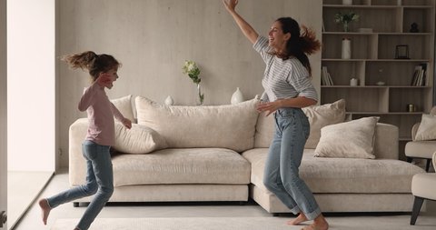 Lively latina mother cheery preschool daughter dancing jumping in cozy modern living room. Carefree happy family enjoy active weekends listen music moving indoor. Home hobby, fun and leisure concept