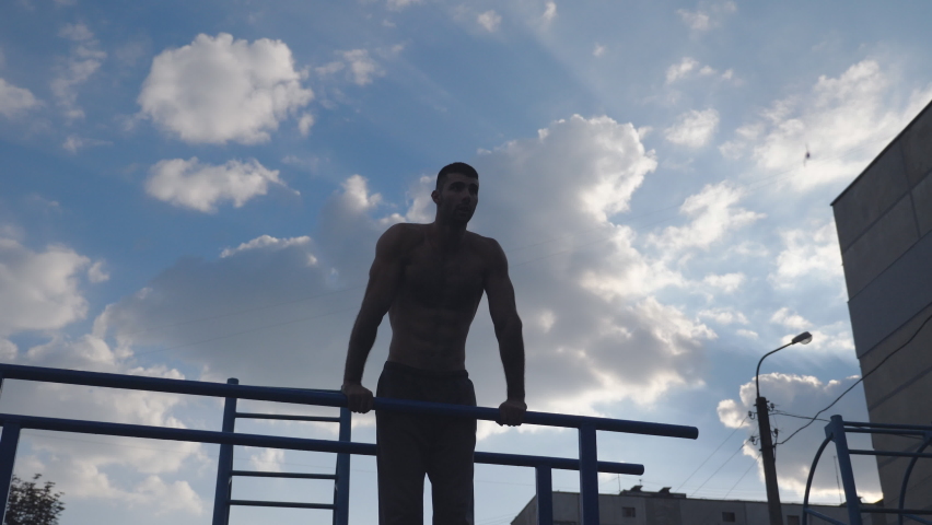 Muscular man doing push ups on parallel bars at sports ground. Young athlete exercising at playground. Strong sporty man training outdoor. Concept of healthy and active lifestyle. Low view