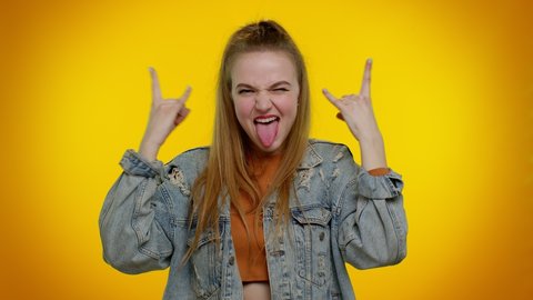 Rock n roll. Overjoyed delighted sincere teen girl 20s years old in denim jacket showing gesture by hands, cool sign, shouting yeah with crazy expression, dancing, emotionally rejoicing in success win