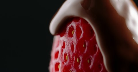 Ripe red juicy strawberry being slowly covered with hot molten chocolate. Tasty snack on black background food and drink close up 4k footageの動画素材