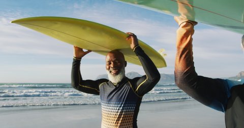 Senior african american couple walking with surfboards at the beach. healthy outdoor leisure time by the sea.