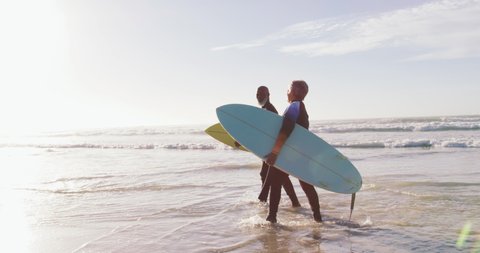 Senior african american couple walking with surfboards at the beach. healthy outdoor leisure time by the sea.
