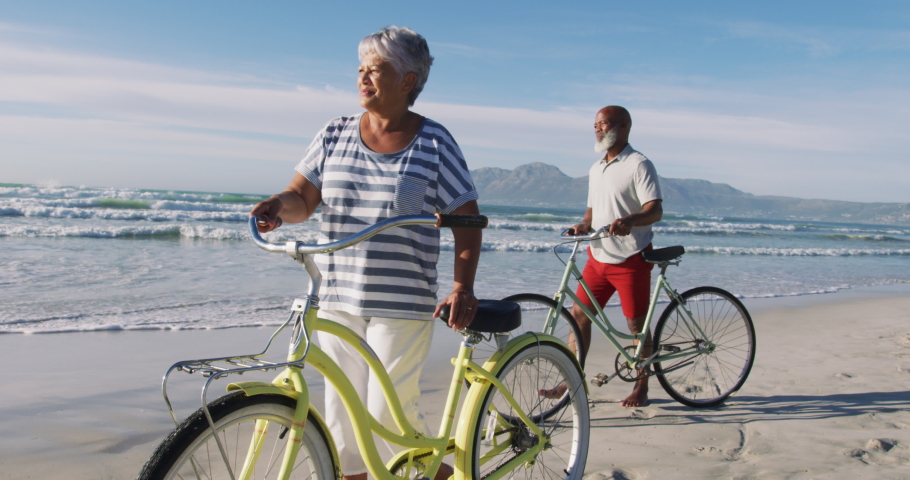 Smiling senior african american couple walking with bicycles at the beach. healthy outdoor leisure time by the sea. Royalty-Free Stock Footage #1071482005