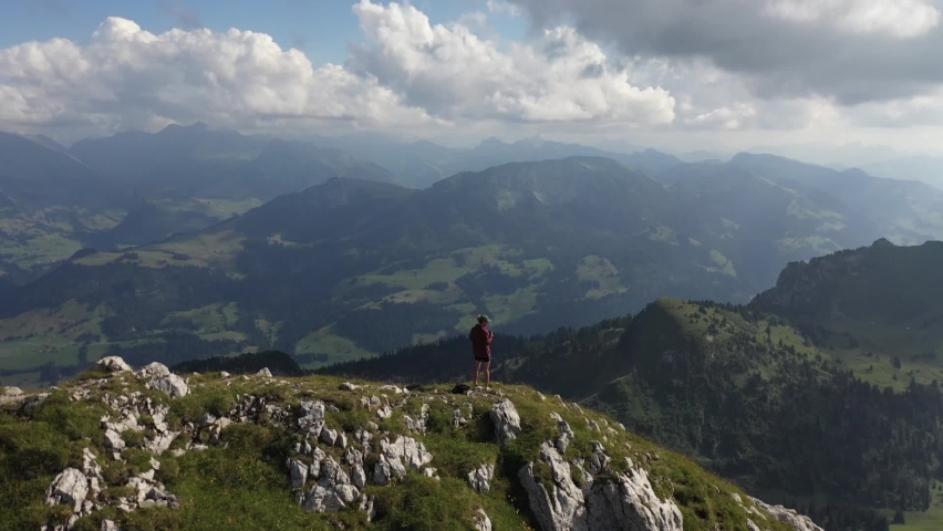 Young man standing by himself alone, taking photos with his camera over the majestic, dramatic and amazing view. Dramatic white clouds, sunbeams and sun rays and a small lake in the wild.