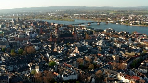 right to left dronee showing the Cathedral of Mainz in the middle of tiny houses on a warm spring day with the Rhine river in the back