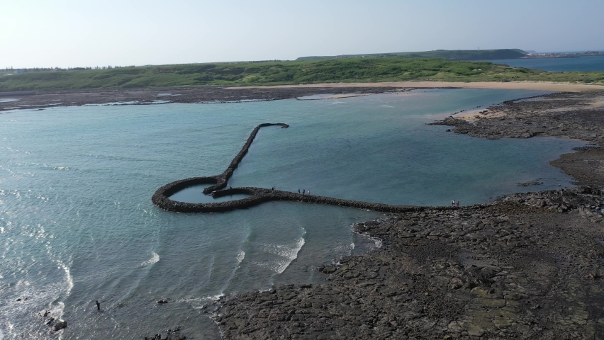Aerial view of the One-Heart Stacked Stones (Eye of Tiger Fish Trap) bathed in the turquoise sea water, which is a traditional fishing weir and a popular tourist attraction, in Xiyu, Penghu, Taiwan Royalty-Free Stock Footage #1071483832