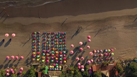 Top down aerial drone footage of one of the famous beach bars in Kuta beach in Seminyak in Bali, Indonesia with their bean bags and colorful umbrellas