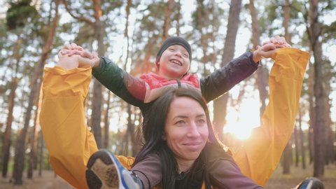 Happy family concept. Happy little boy and mother playing together outdoor enjoy beautiful sunset in the pine forest. Mother holds her son on the neck. Helping hand. Teamwork and friendly family.