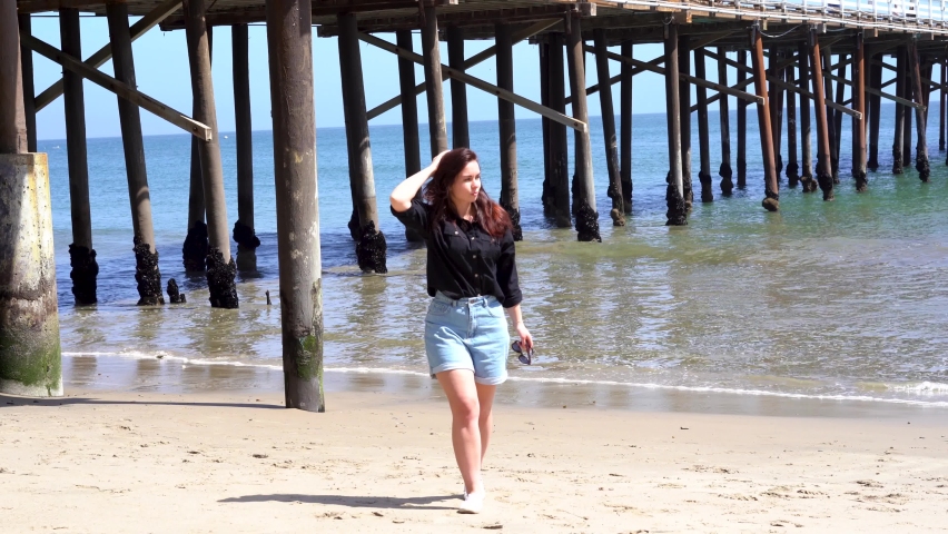 A young girl walks in the sand on camera near Malibu Pier in Los Angeles, California