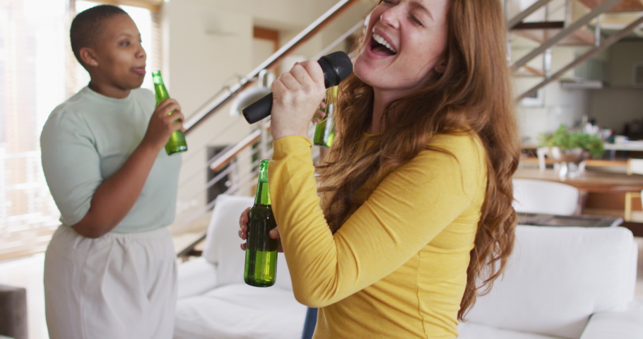 Diverse group of female friends having fun singing karaoke and drinking beer at home. female friends hanging out enjoying leisure time together. Royalty-Free Stock Footage #1071491467