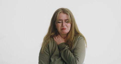 Unhappy plump blonde woman in green sweatshirt cries hugging herself with offence on white background close view slow motion