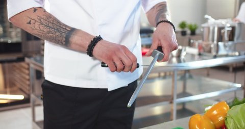 Close up of professional male cook hands sharpening knife. Man chef preparing knife tool for work. Working in restaurant kitchen. Cookery, culinary, cafeteria kitchen, occupation concept