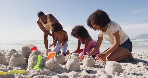African american parents and their children playing with sand on the beach. family outdoor leisure time by the sea.