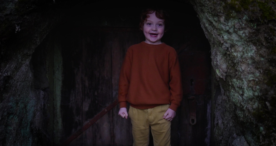 happy redhead boy is going out from an old rusty door in the woods. five years old kid