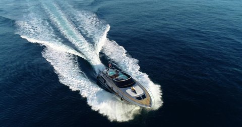 Aerial view of a yacht sailing at full speed, with a man resting in the front of the boat