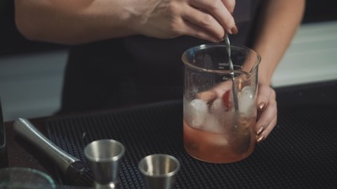 Speakeasy bartender making cocktail, stirring liquor with bar spoon.