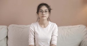 POV of A young beautyful glasses asian woman sit on sofa and looking to camera for work or study online. Pretty girl in casual clothes at house during quarantine. Social distance new normal concept.