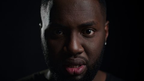 Closeup african american man crying on black background. Portrait of frustrated male person looking at camera in studio. Shocked afro guy yelling indoors.