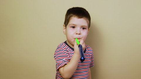 A small child plays on a flute toot and laughs on a beige background. A cheerful boy celebrates birthday, blowing in a flute tongue-shaped whistle, children's joy. Toy store for children