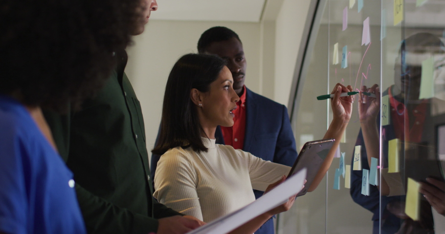 Diverse group of colleagues in meeting room mixed race businesswoman writing notes on glass wall. business in a modern office. Royalty-Free Stock Footage #1071505894