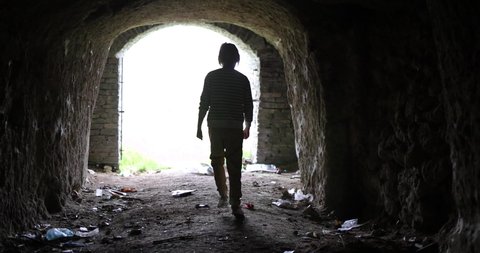 silhouette of boy walking to the light from dark dirty dungeon