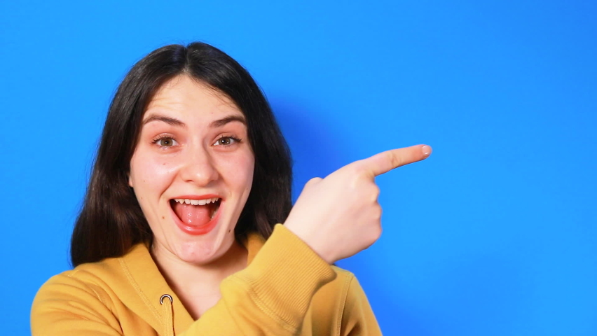 A brunette woman shows her finger to the side, sideways and laughs, screams with joy. Videos for advertising about discounts, sales or lotteries.