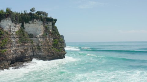 Stunning tropical coastline and blue ocean in Bali, Indonesia. Aerial view of large waves crashing in rocky cliffs in Bali