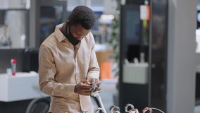 afro-american man with face mask is testing smartwatch in electronics store, buying modern device in large shop