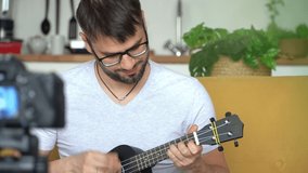 Portrait of young male smiling blogger records video on camera, playing guitar at home. Online music teaching concept. Ukulele