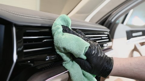 Side view of man taking care of car interior in garage. Cleaning dashboard with a microfiber.