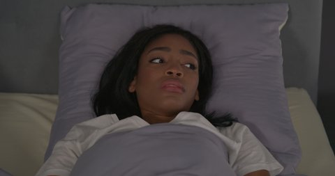 African American woman lying in bed at night and wakes up from nightmare or sudden restless thought. Scared facial expression