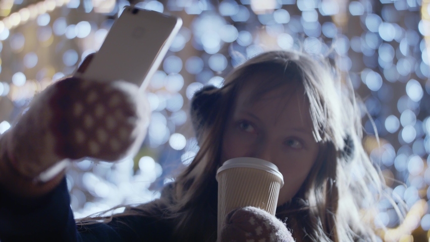 Joyous polish woman in winterwear trying to click a selfie sipping coffee