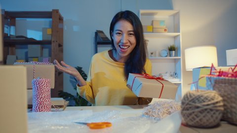 Happy young Asia businesswoman looking at camera selling  introduce product to client video live streaming in online shop  marketplace at night. Small business owner, online market delivery concept.