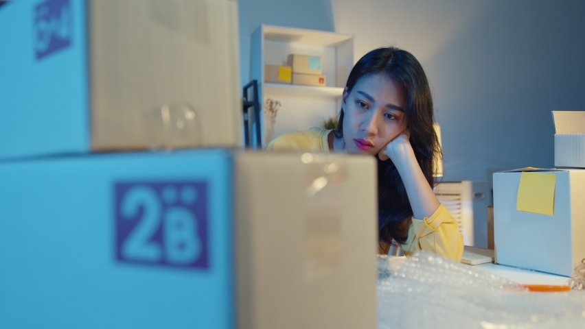 Young Asia businesswoman look around room full of product stuff and parcel box feel stress and upset with bad sell in home office at night. Small business owner, online market delivery concept. Royalty-Free Stock Footage #1071531571
