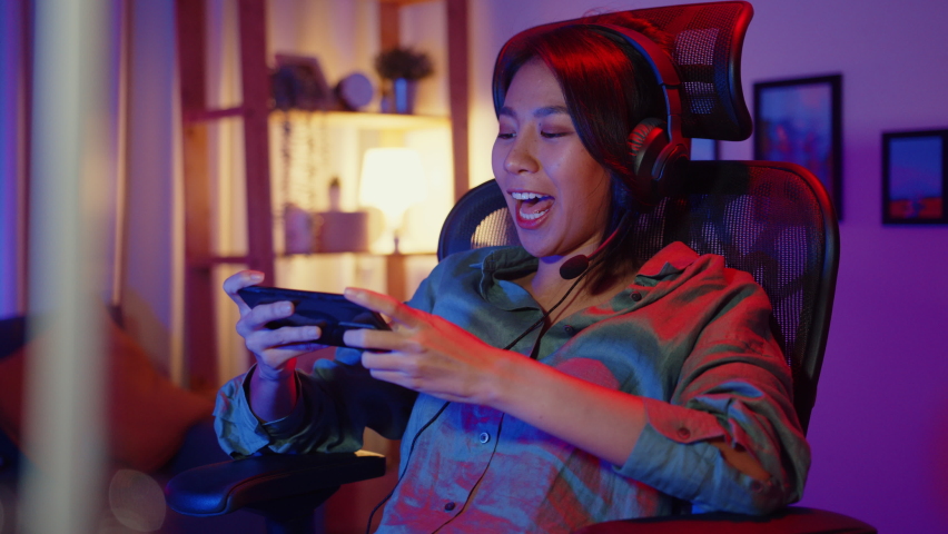 Happy asia girl gamer wear headphone competition play video game online with smartphone colorful neon lights in living room at home. Esport streaming game online, Home quarantine activity concept. Royalty-Free Stock Footage #1071531604