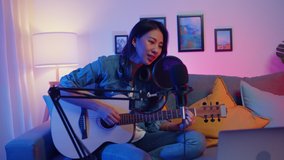 Happy asia girl blogger play guitar and use microphone sing song record music sound mixer on laptop in modern living room home studio at night. Music content creator, Tutorial, Broadcast concept. - Powered by Shutterstock - Get 15% off with code: PIKWIZARD15
