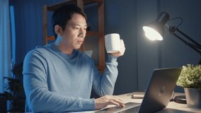 Asia businessman take a break with a cup of coffee relax and checking work assignment at laptop computer for agenda in living room at home overtime at night, Work from home corona pandemic concept. - Powered by Shutterstock - Get 15% off with code: PIKWIZARD15