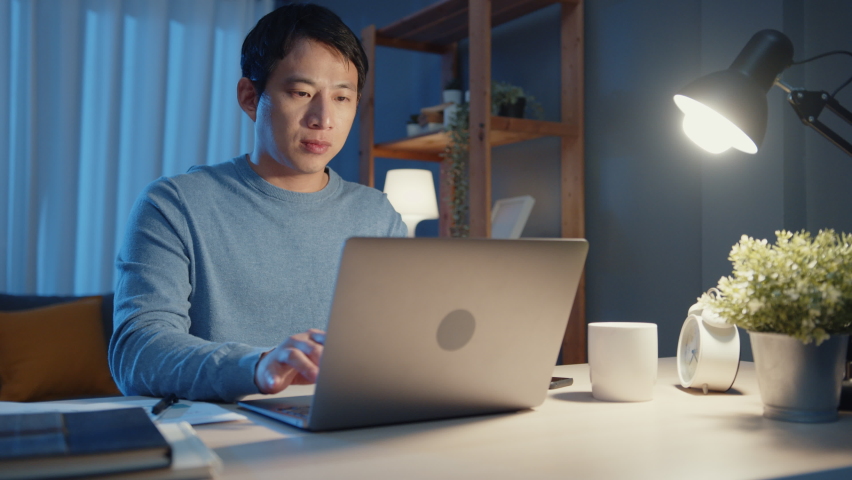 Asia freelance businessman focus working typing on laptop computer online remotely from company on desk in living room at home overtime at night, Work from home during COVID-19 pandemic concept. Royalty-Free Stock Footage #1071531775