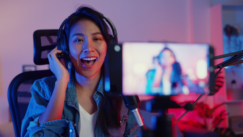 Happy asia girl blogger music influencer use smartphone broadcast recording wear headphone online live talk with listening audience in living room home studio at night. Content creator concept. Royalty-Free Stock Footage #1071531787