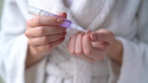 Closeup female hands are holding little bottle with nourishing cuticle oil. Young woman girl is smearing her nails, making herself hygienic manicure. Personal hygiene and care products concept.