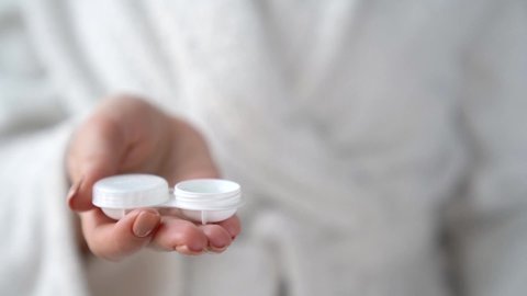 Closeup female hands are holding white plastic container for contact lenses. Woman is pouring cleaning liquid water for washing soft optical lens. Vision correction of myopia, hyperopia concept.