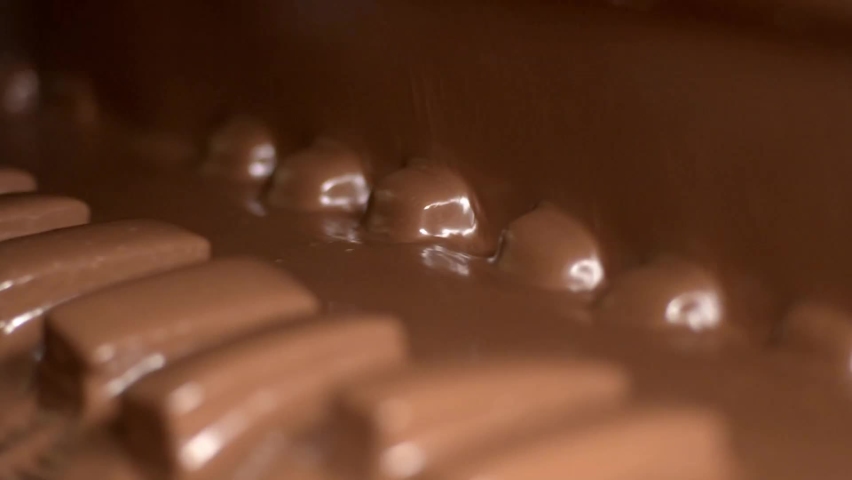 It is poured over the cakes with chocolate. Nougat and peanut chocolate production. The chocolate bars move along the conveyor belt in the confectionery factory for confectionery production.  Royalty-Free Stock Footage #1071534148