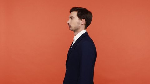 Positive confident successful young bearded man in business suit turning to camera, smiling and crossed arms, looking at camera with optimism. Indoor studio shot isolated on orange background