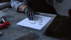 Rolling linoleum in a form of bird to make a pressure on a piece of paper. Linocut concept. Male in black gloves rolling on cut stamp to make a print on paper. High quality 4k video footage