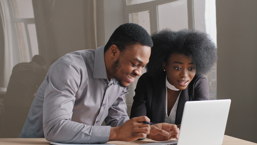 Young african american office workers, guy and girl, work successfully together with concentration laptop computer in office. Happy satisfied business woman and man receive good news letter, rejoice | Shutterstock HD Video #1071542140