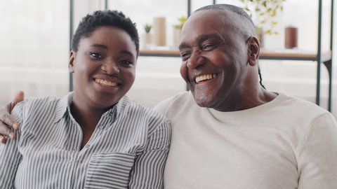 Family portrait african couple different ages afro young woman and mature black ethnic man sitting on couch talking laughing. Senior father and mixed race daughter looking at camera chatting cuddling
